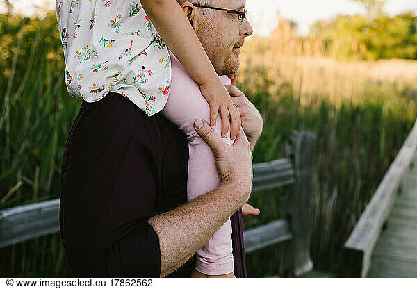Father gives daughter a ride on shoulders in golden light