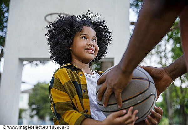 Father giving basketball to daughter at sports court