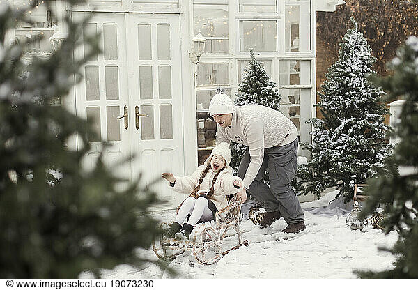 Father giving ride to daughter on sledge outside house