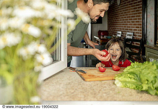Father having fun with son playing with tomatoes at home