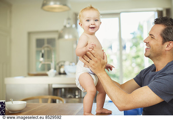 Father helping baby walk on table
