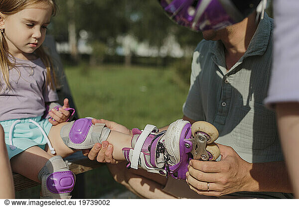 Father helping daughter in putting roller skates at park