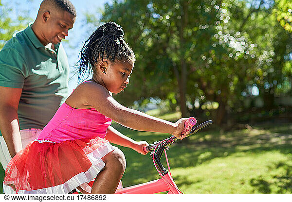 Father helping daughter learn to ride bike in sunny summer park
