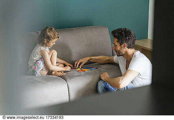 Father helping daughter while playing with puzzle on sofa