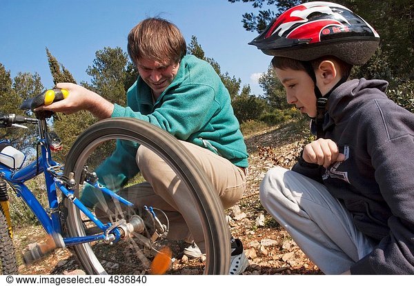 Father helping his son repair the flat tyre of his mountain bike