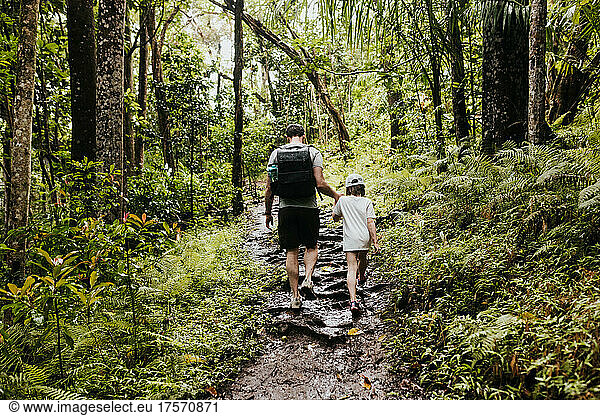 Father helps daughter up a hill while hiking in Hawaiian forest