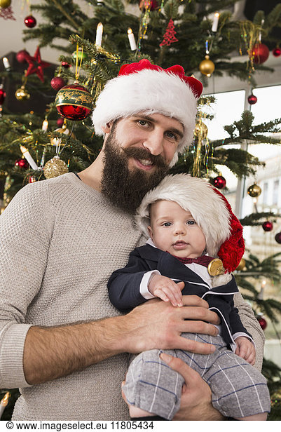 Father holding baby boy against Christmas tree