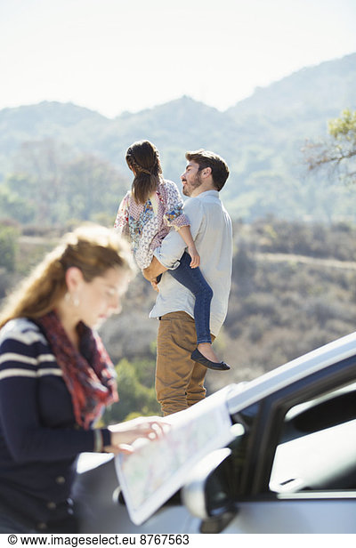 Father holding daughter at roadside while woman checks map