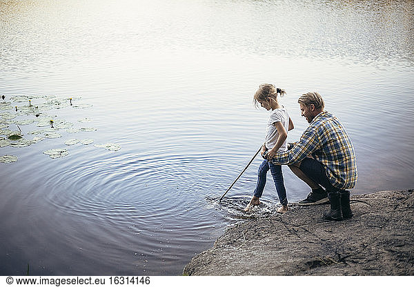 Father holding daughter during fishing by lake
