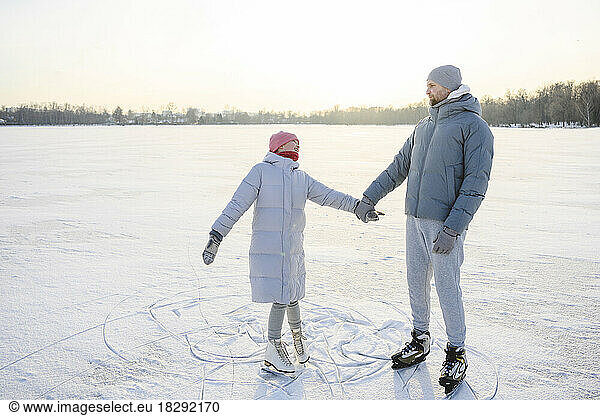 Father holding hands of daughter and practicing ice skating on winter lake