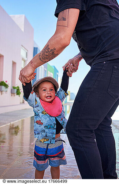 Father holding hands with cute toddler boy on street