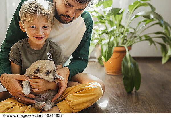 Father holding son and cute puppy on floor at home