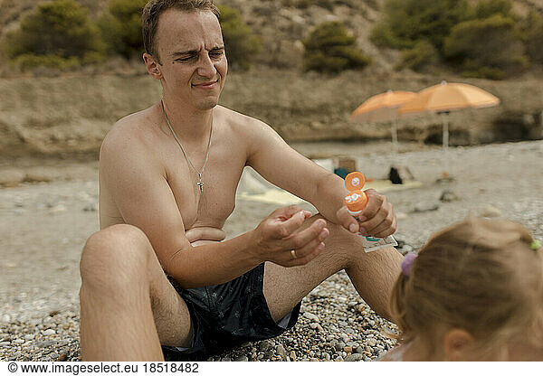 Father holding suntan lotion with daughter at beach