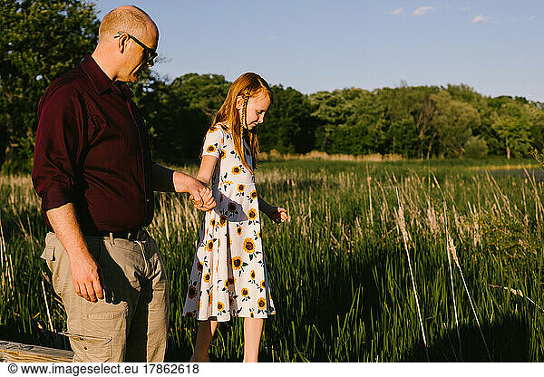 Father holds daughters hand while walking in nature