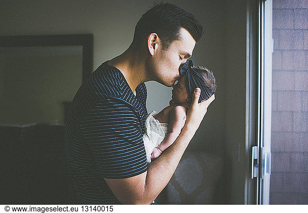 Father kissing on newborn daughter's forehead at home