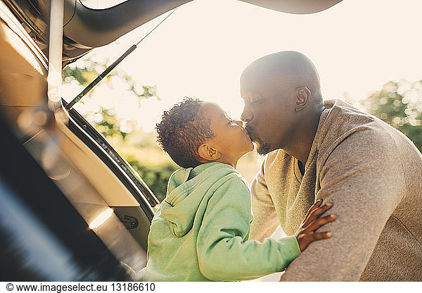 Father kissing son sitting in car trunk