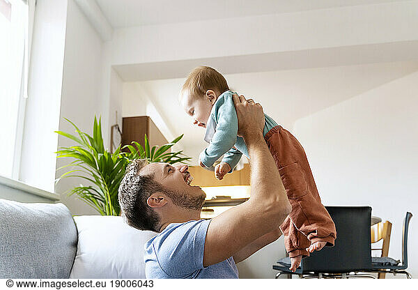 Father lifting cute baby boy in living room at home