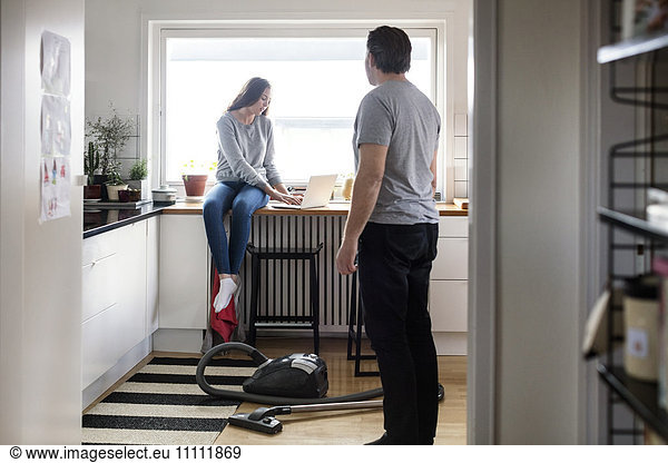 Father looking at daughter using laptop on kitchen counter in new house