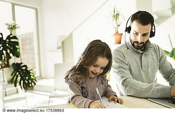 Father looking at smiling girl drawing on book