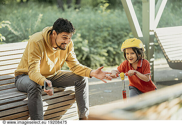 Father looking at son riding push scooter at park