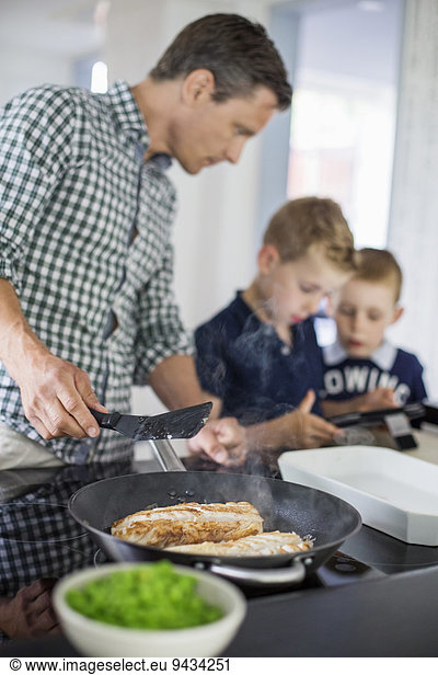 Father looking at sons using digital tablet while preparing food in kitchen