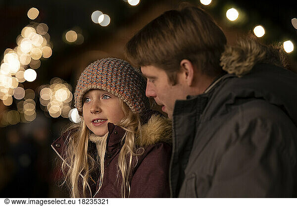 Father looking at thoughtful daughter at Christmas market at night