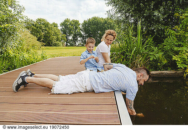 Father lying with family sitting on footbridge over lake