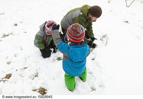 Father making a snowball outside with two children during winter