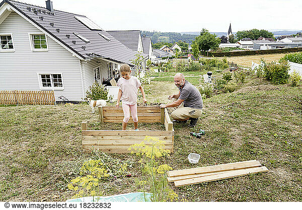 Father making raised bed with daughter in backyard near house