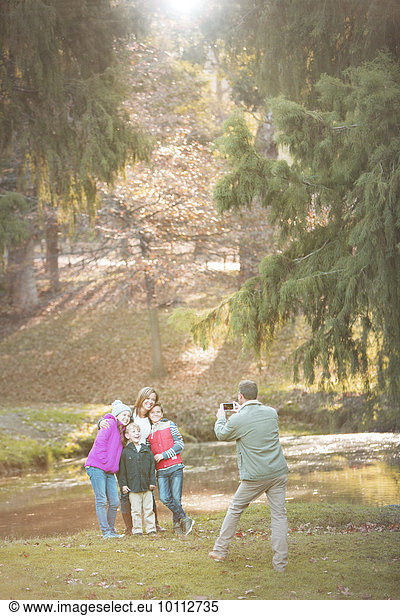 Father photographing family with camera phone in park