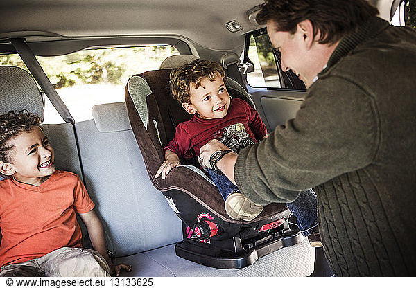 Father placing son on baby seat in car