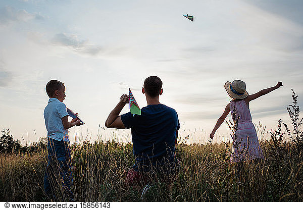 father playing paper aeroplanes with his son and daughter at sunset