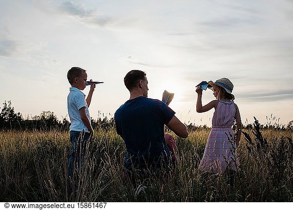 father playing paper aeroplanes with his son & daughter at sunset