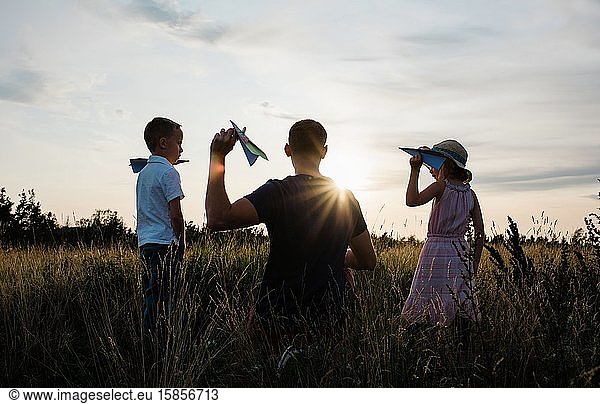 father playing planes with son and daughter in a meadow at sunset