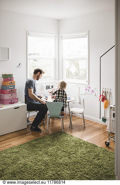 Father playing with daughter at small dining table in playroom