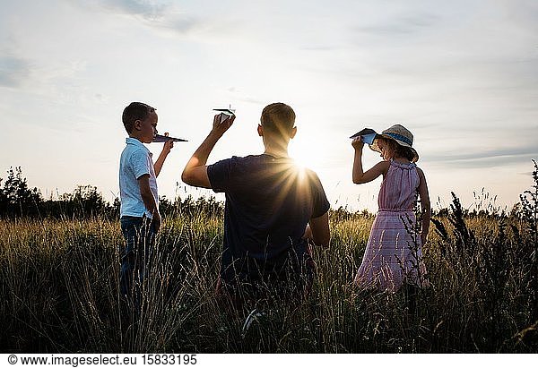 father playing with his son and daughter in a meadow at sunset
