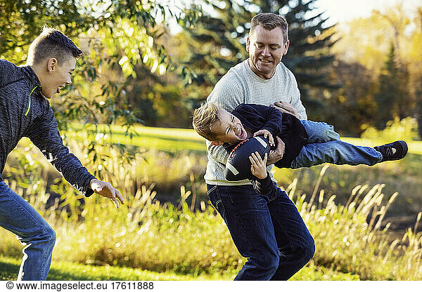 Father playing with his two sons in a park in autumn; St. Albert  Alberta  Canada