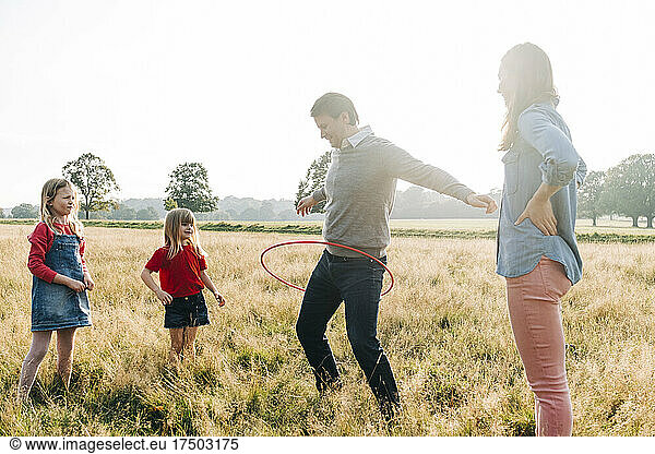 Father playing with hula hoop by mother and daughters in park