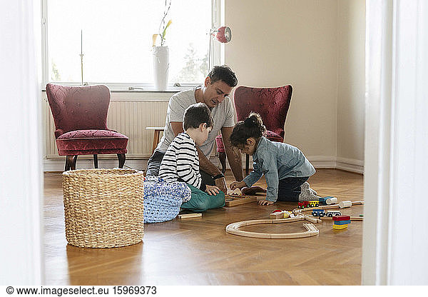 Father playing with son and daughter in living room at home
