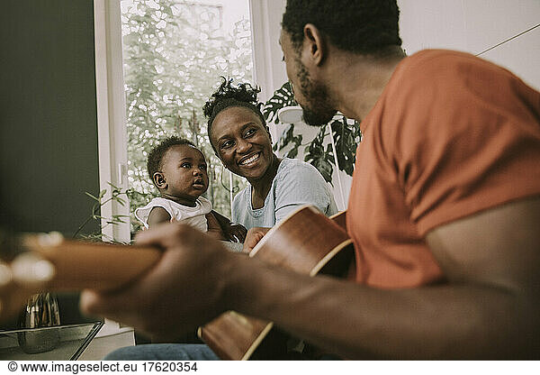 Father plucking guitar by son and mother in living room