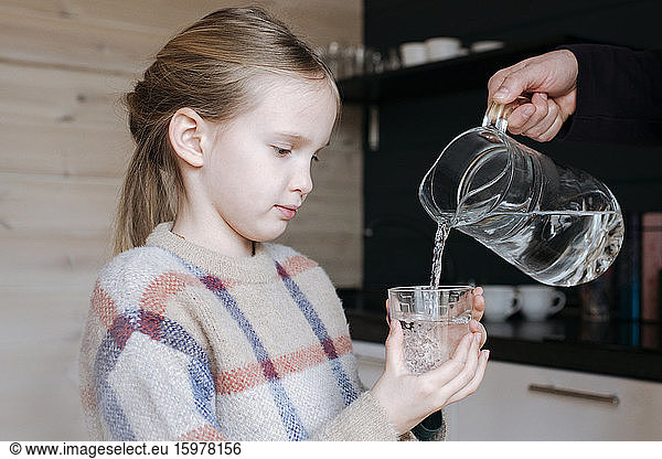Father pouring water into glass for his daughter in the kitchen