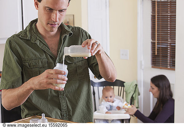 Father preparing baby's formula and mother feeding baby