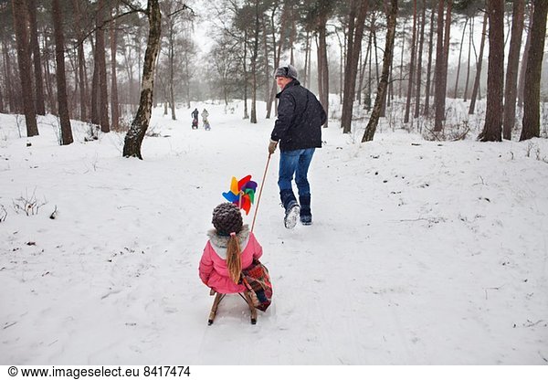 Father pulling daughter on toboggan in snow