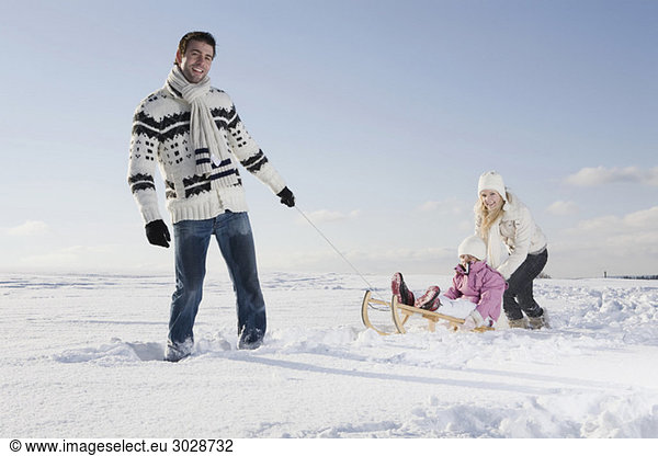 Father pulling girl (6-7) on sledge Mother backing daughter