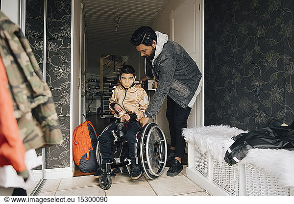 Father pushing autistic son sitting on wheelchair in corridor at home
