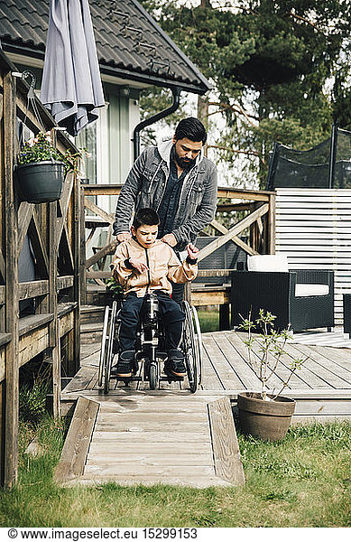 Father pushing autistic son sitting on wheelchair in yard