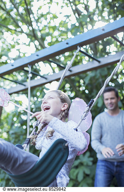 Father pushing daughter on swing outdoors