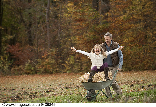 Father pushing happy daughter in wheelbarrow