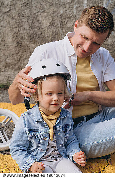 Father putting on a safety helmet for daughter to ride balance bike