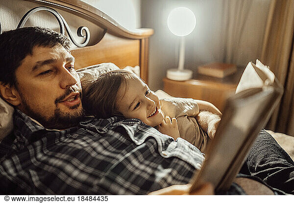 Father reading book lying on bed with son at home